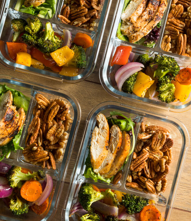 Sliced chicken on greens, mixed vegetables, and pecan nuts on a glass meal prep containers