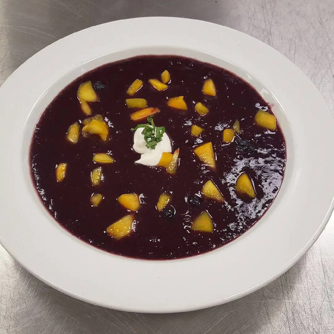 A bowl of fruit soup topped with peaches and sour cream