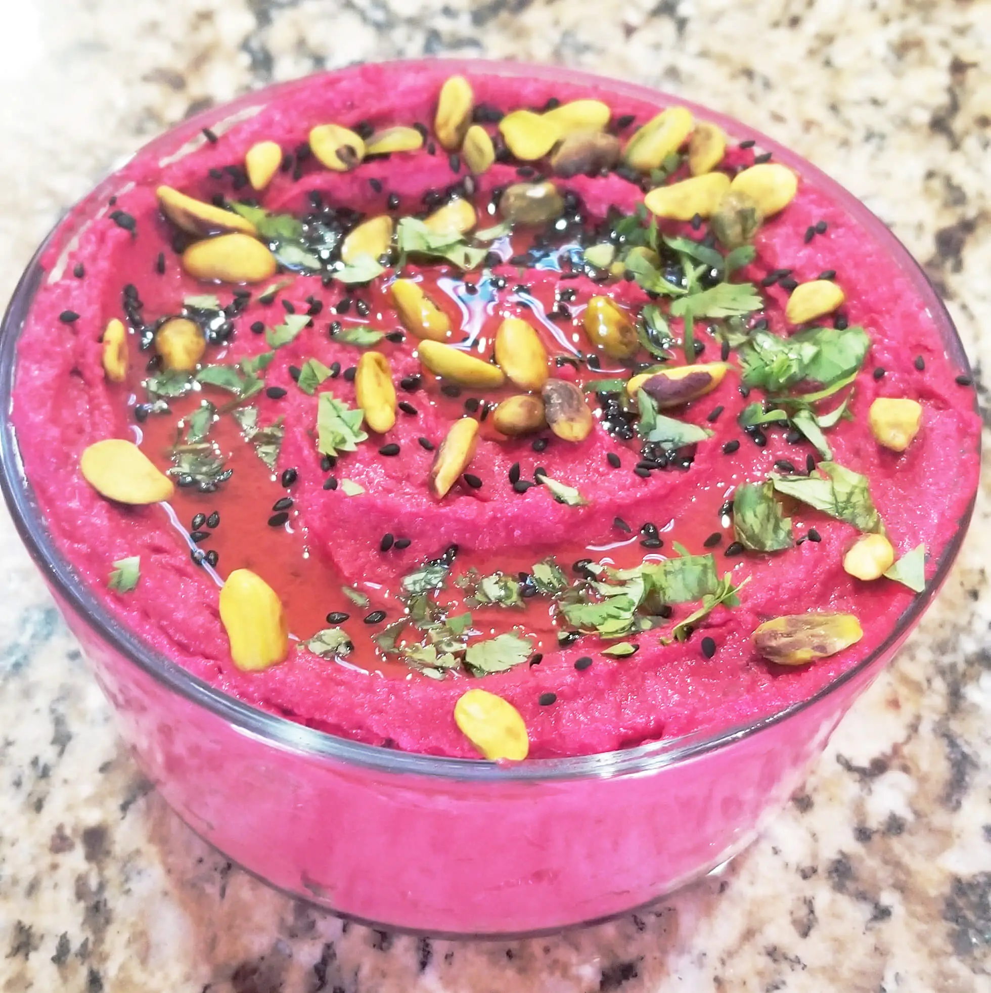 A bowl of roasted beet dip adorned with a variety of nuts and seeds, creating a visually appealing and nutritious culinary delight.
