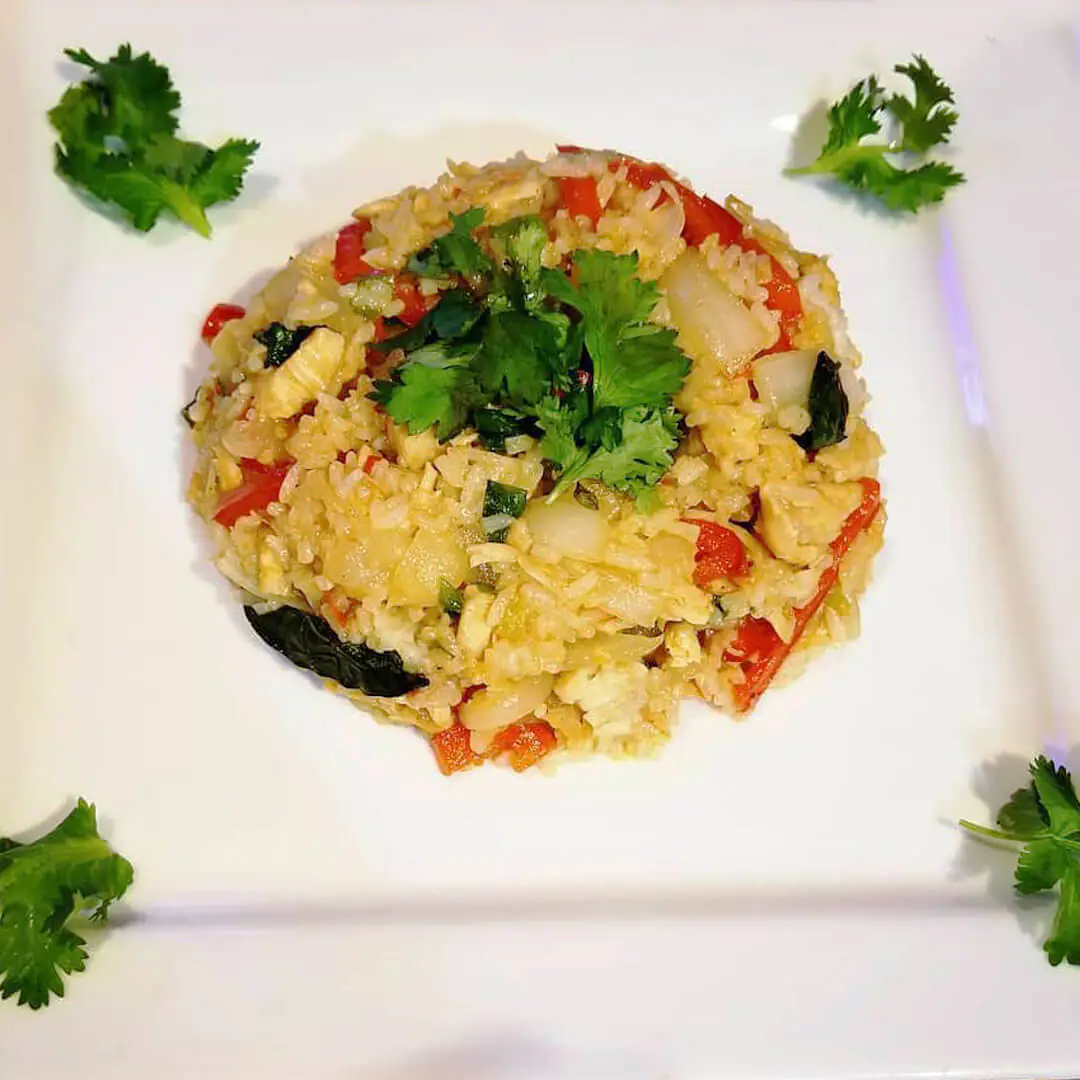 A plate of chicken fried rice showcasing basil leaves and vegetables, topped with parsley