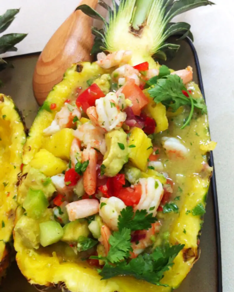 An appetizing blend of shrimp, pineapple, avocado, and tomatoes within a hollowed-out pineapple shell